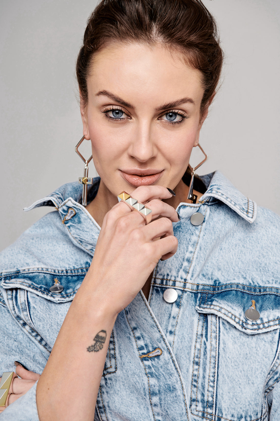 Close up image of Cirkl statement accessories featuring sterling silver and 18k gold mixed metals. Model looking straight at the camera with hands framing her face to help feature the jewellery. Styled with an oversized denim jacket and hair pulled back t
